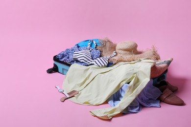 Open suitcase with traveler's belongings on pink background, space for text