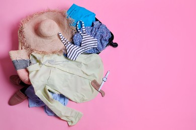 Open suitcase with traveler's belongings on pink background, top view. Space for text