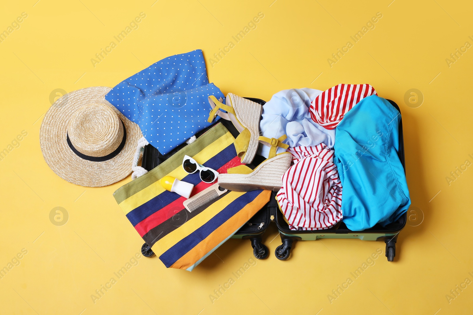 Photo of Open suitcase with traveler's belongings on yellow background, top view