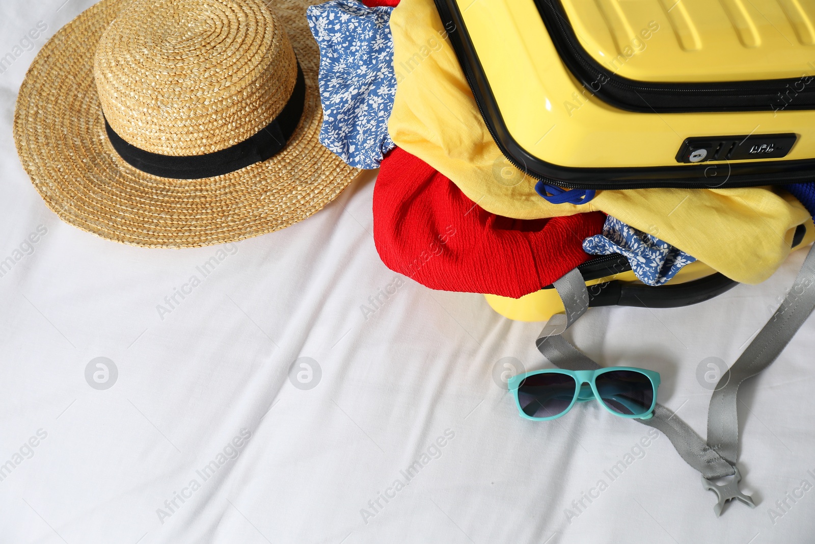 Photo of Open suitcase with traveler's belongings on bed, above view. Space for text