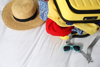 Open suitcase with traveler's belongings on bed, above view. Space for text