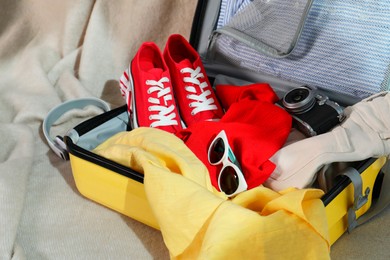 Open suitcase with traveler's belongings on bed, closeup