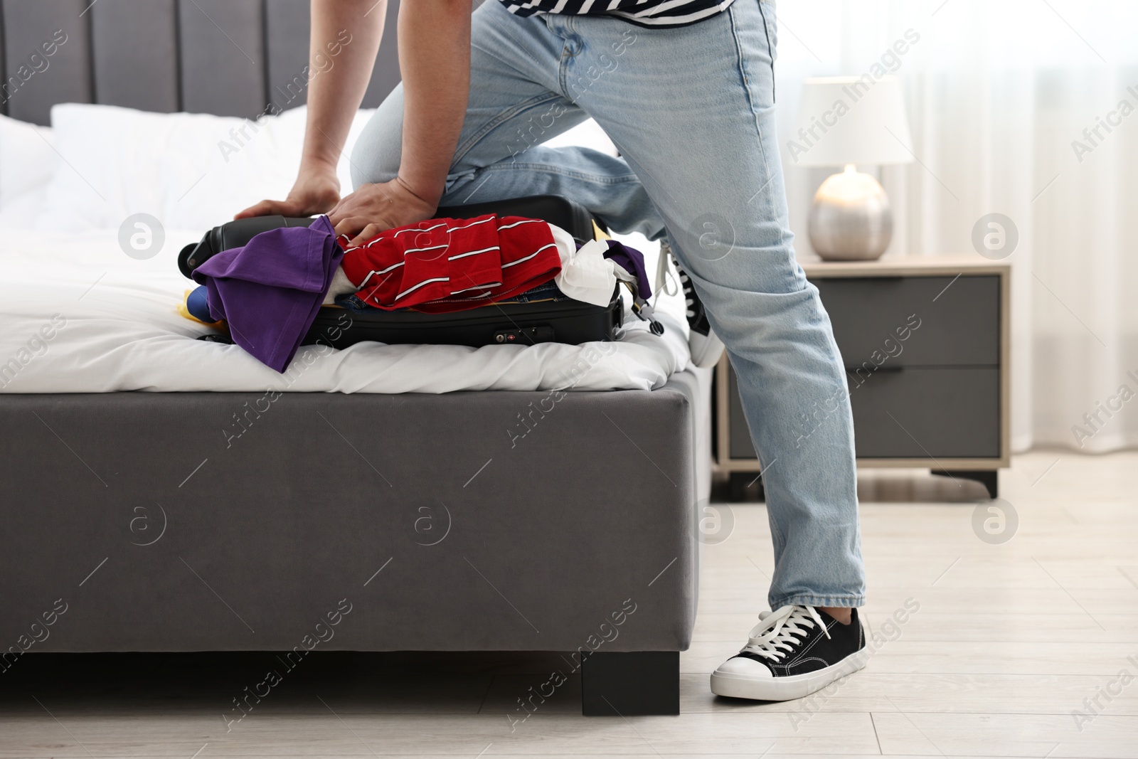 Photo of Man packing suitcase for trip in bedroom, closeup