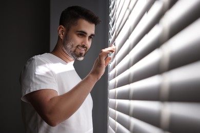 Photo of Man near window blinds at home, space for text