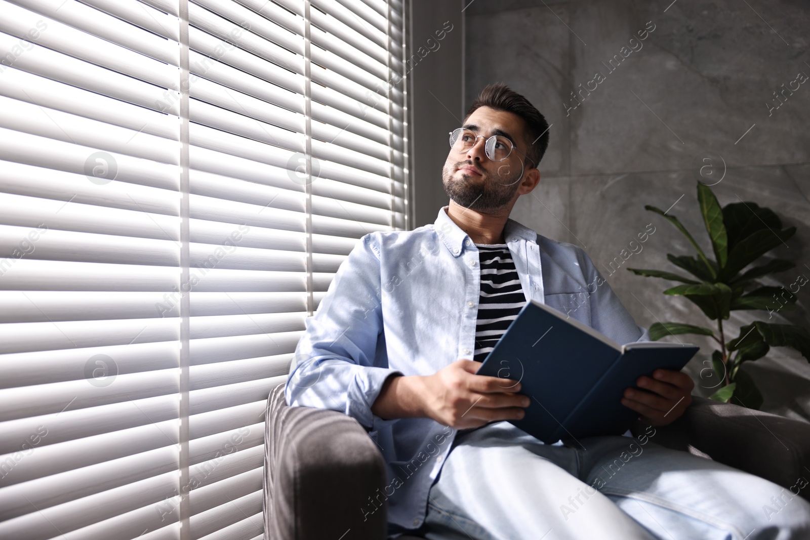 Photo of Man reading book near window blinds indoors, space for text