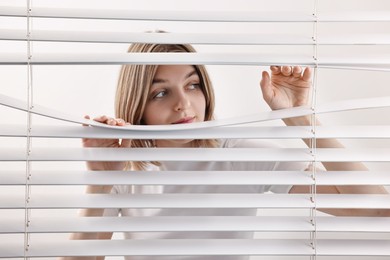 Photo of Young woman looking through window blinds on white background