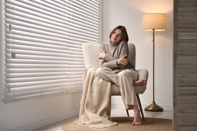 Photo of Woman sitting on armchair near window blinds at home, space for text