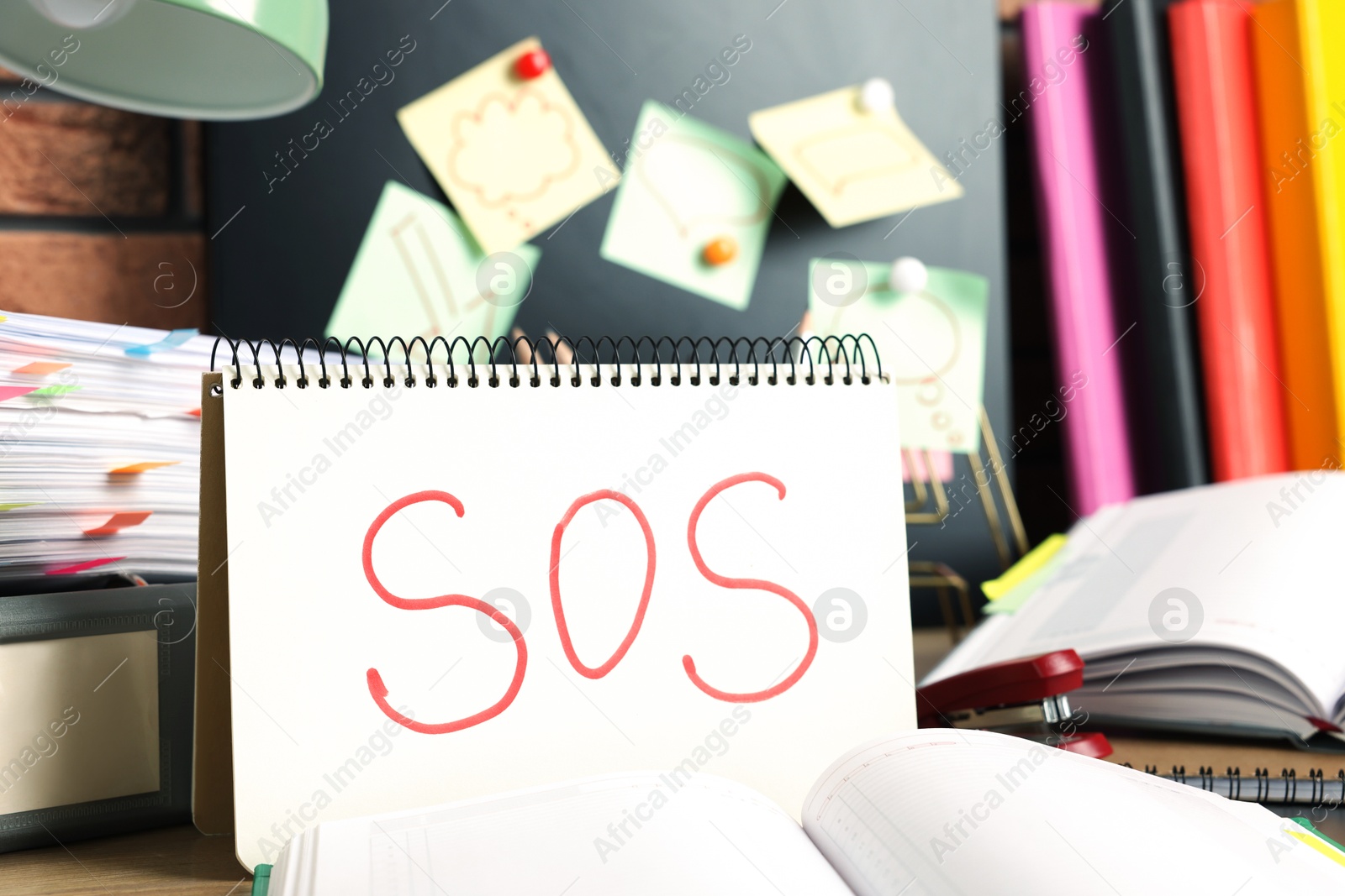 Photo of Notebook with word SOS and stationery on table at workplace