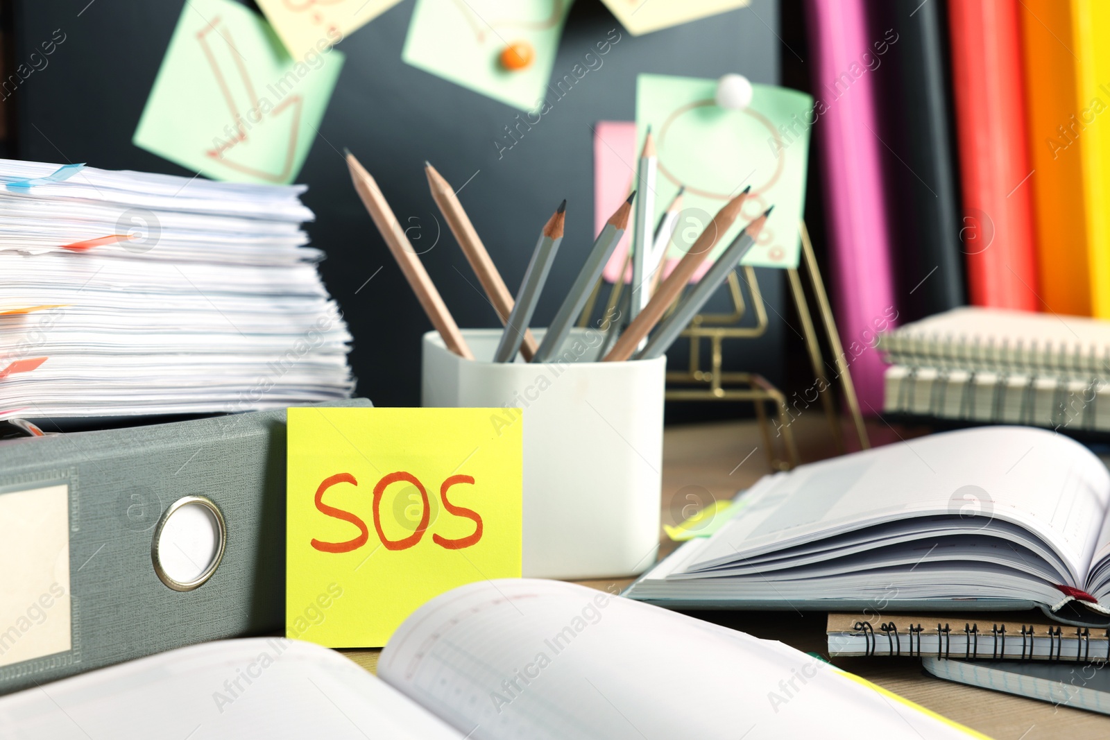 Photo of Sticky note with word SOS and stationery on table at workplace