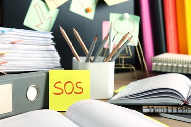 Sticky note with word SOS and stationery on table at workplace