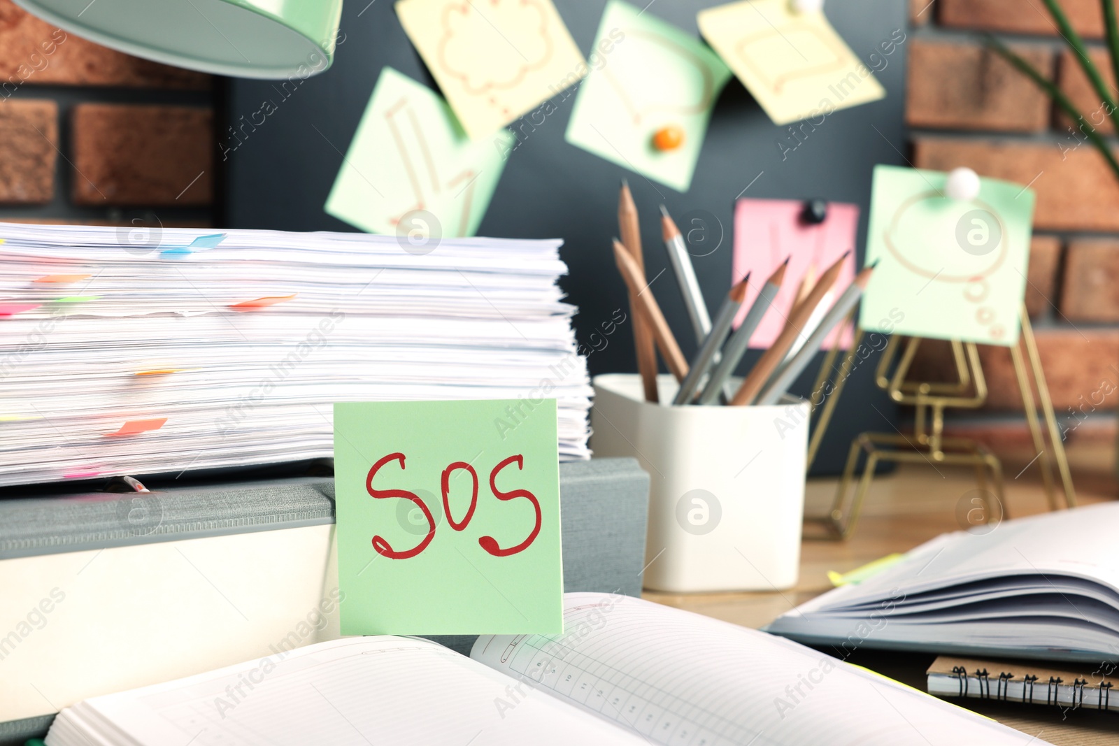 Photo of Sticky note with word SOS and stationery on table at workplace