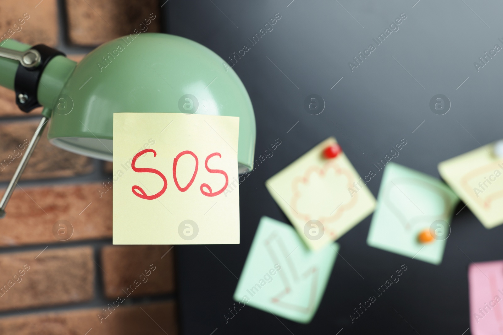 Photo of Sticky note with word SOS on lamp at workplace