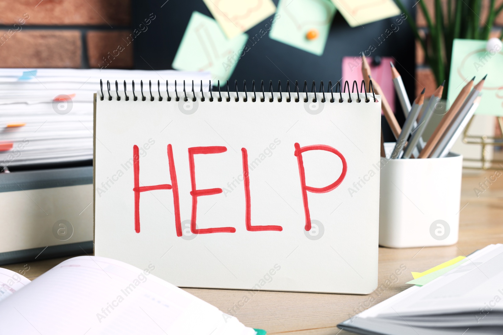 Photo of Notebook with word Help and stationery on wooden table at workplace