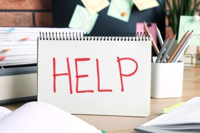 Photo of Notebook with word Help and stationery on wooden table at workplace