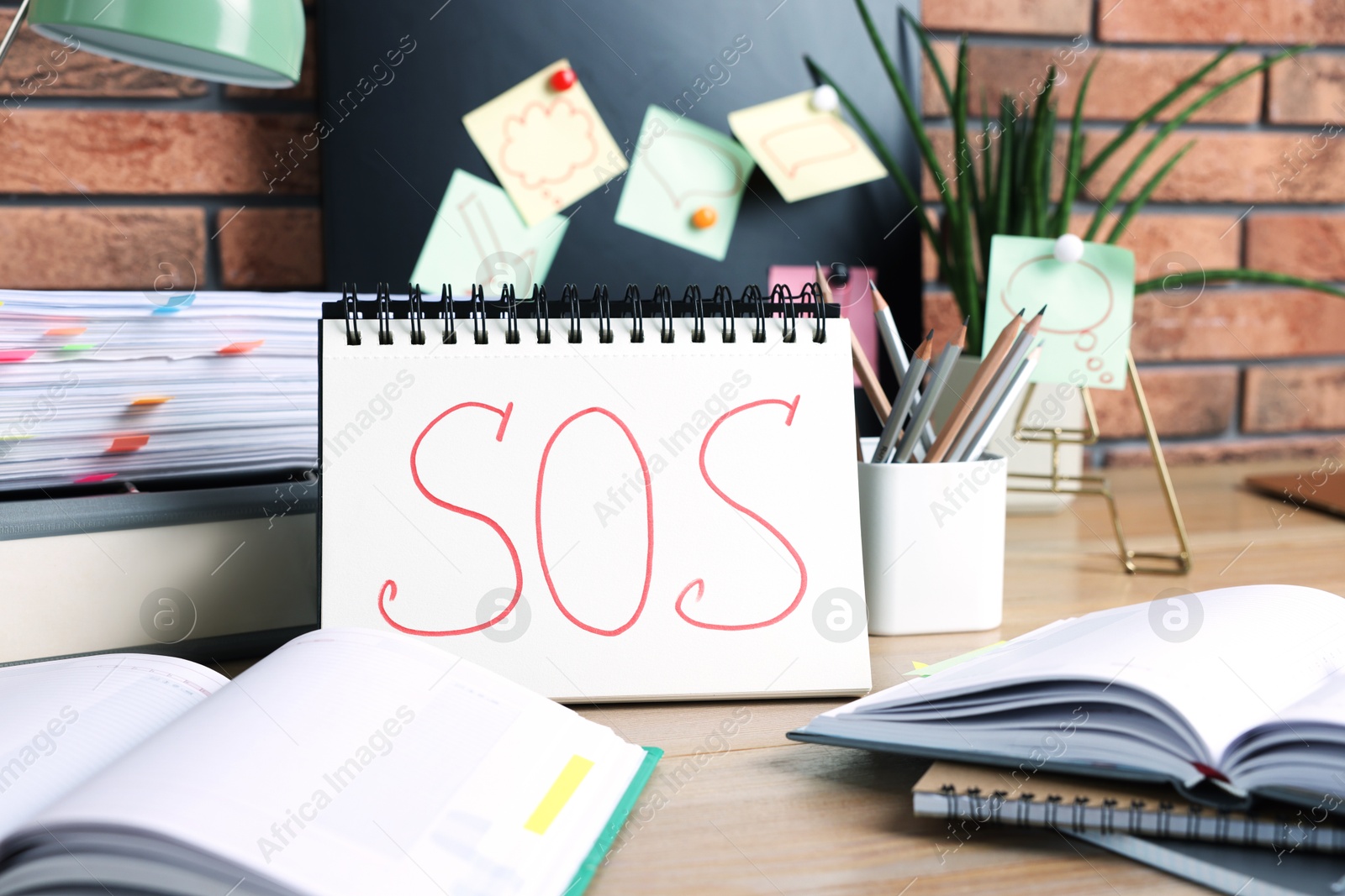 Photo of Notebook with word SOS and stationery on wooden table at workplace