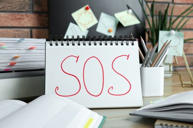 Photo of Notebook with word SOS and stationery on wooden table at workplace