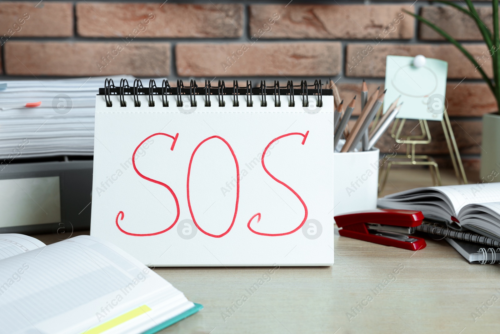 Photo of Notebook with word SOS and stationery on wooden table at workplace