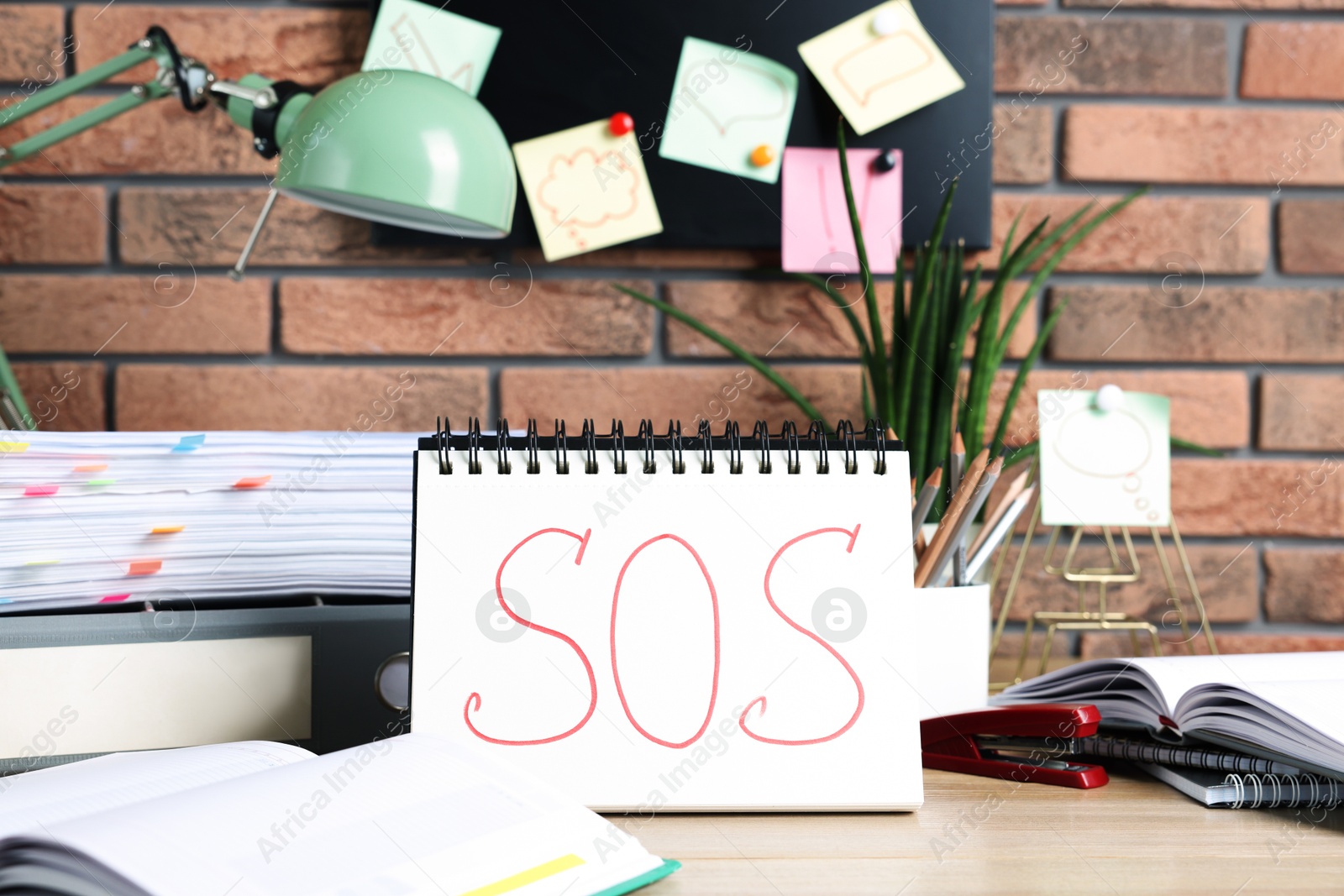 Photo of Notebook with word SOS and stationery on wooden table at workplace