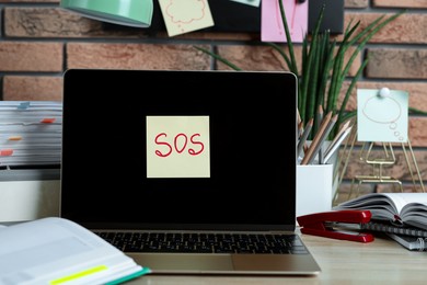 Photo of Sticky note with word SOS, laptop and stationery on wooden table at workplace