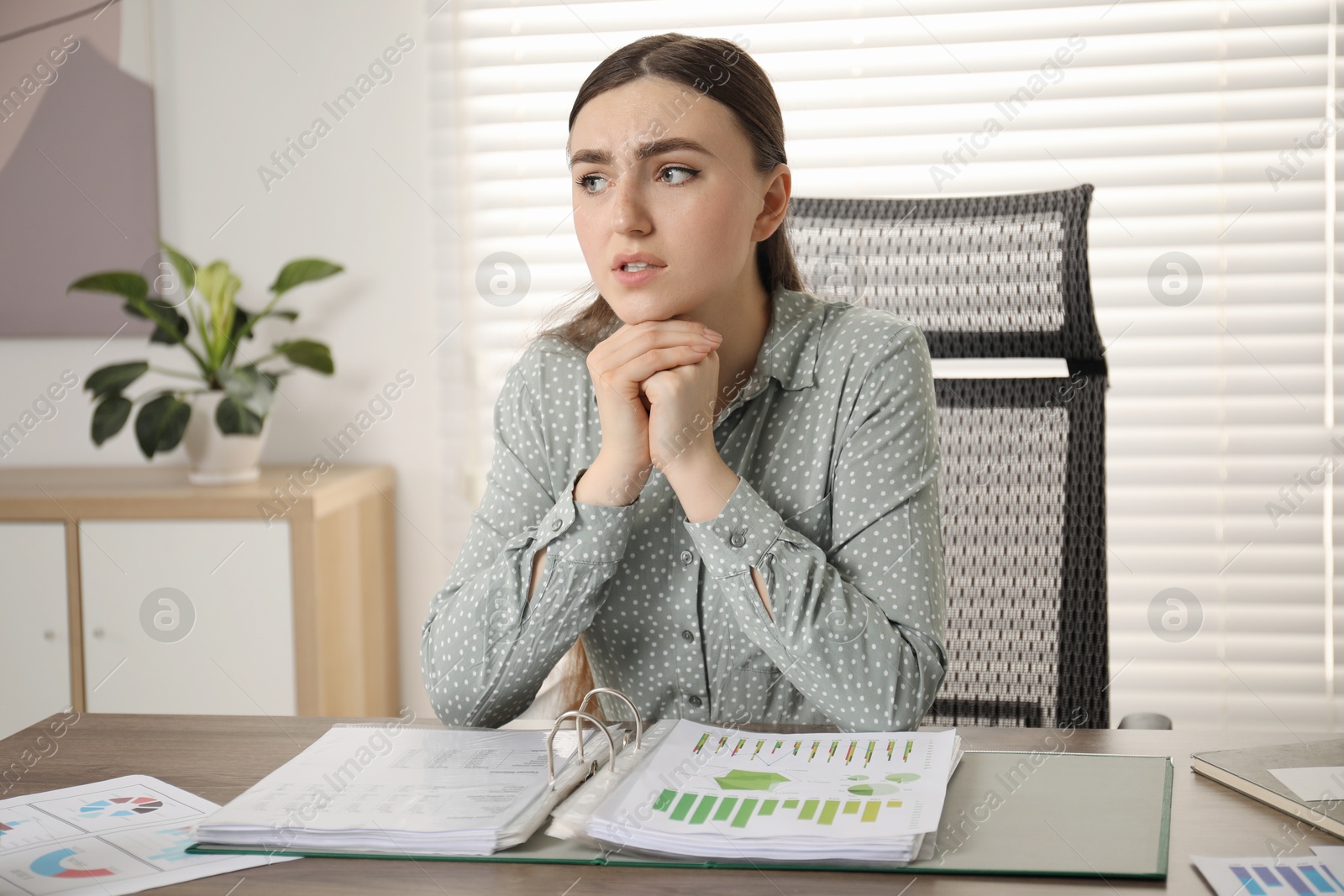 Photo of Embarrassed woman at wooden table with documents in office