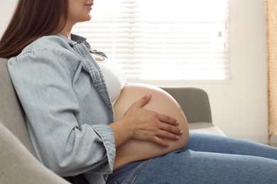 Pregnant woman sitting on sofa at home, closeup