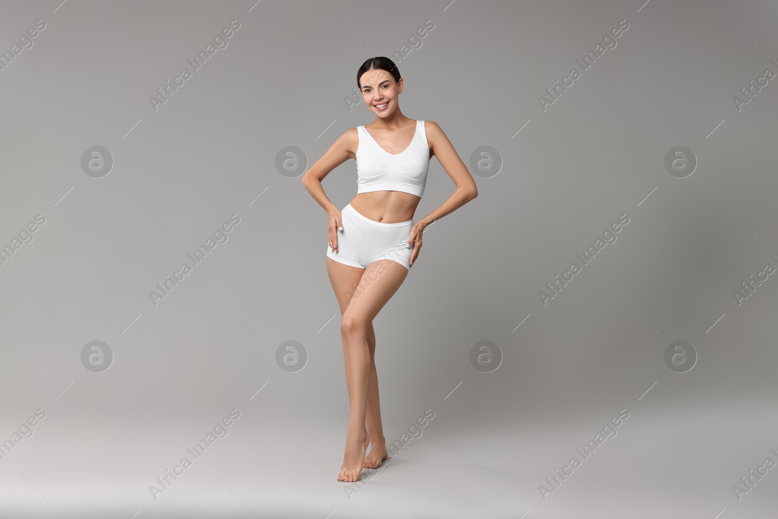 Photo of Smiling woman with perfect skin in underwear on grey background. Body care