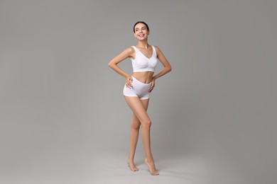 Smiling woman with perfect skin in underwear on grey background. Body care