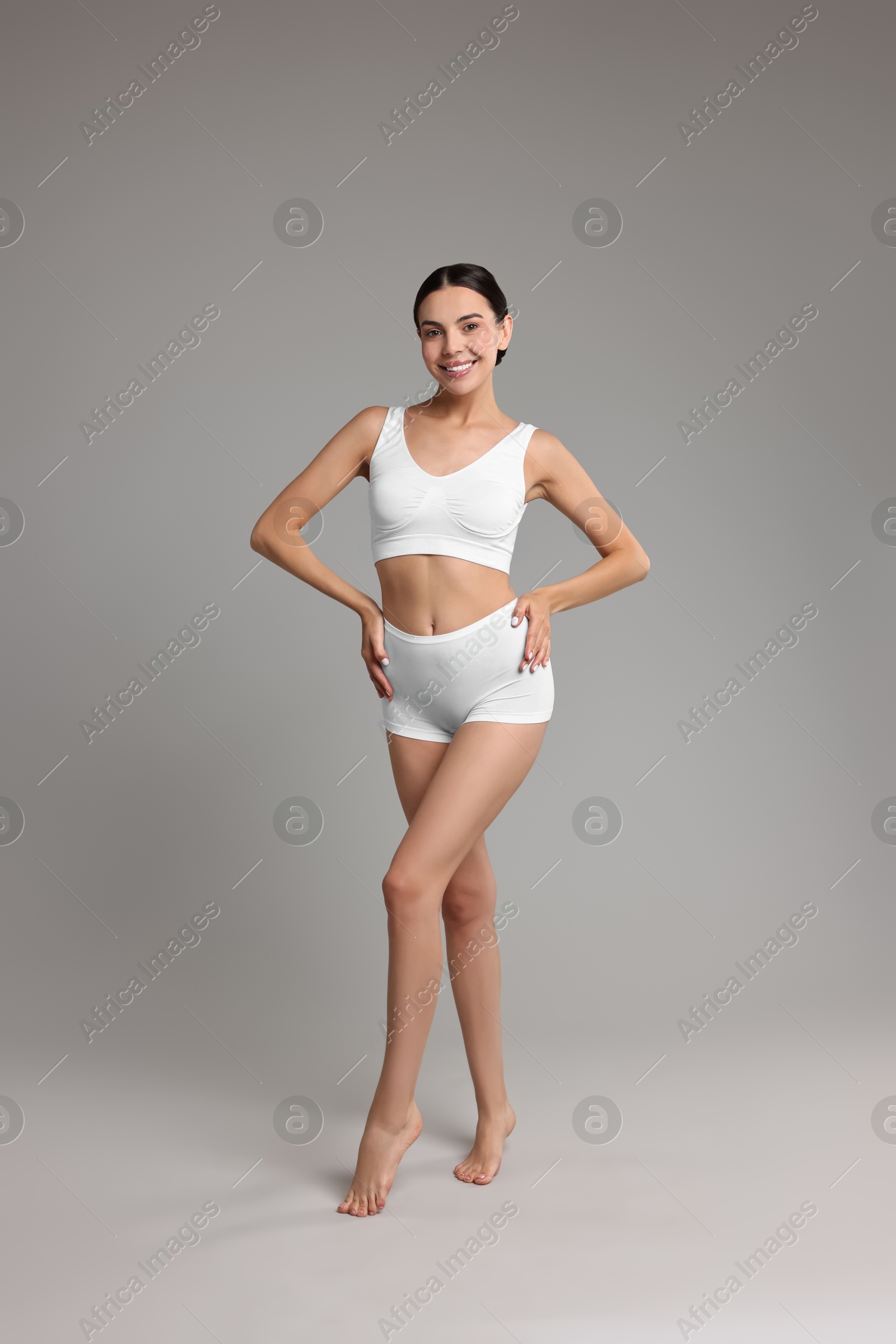 Photo of Smiling woman with perfect skin in underwear on grey background. Body care