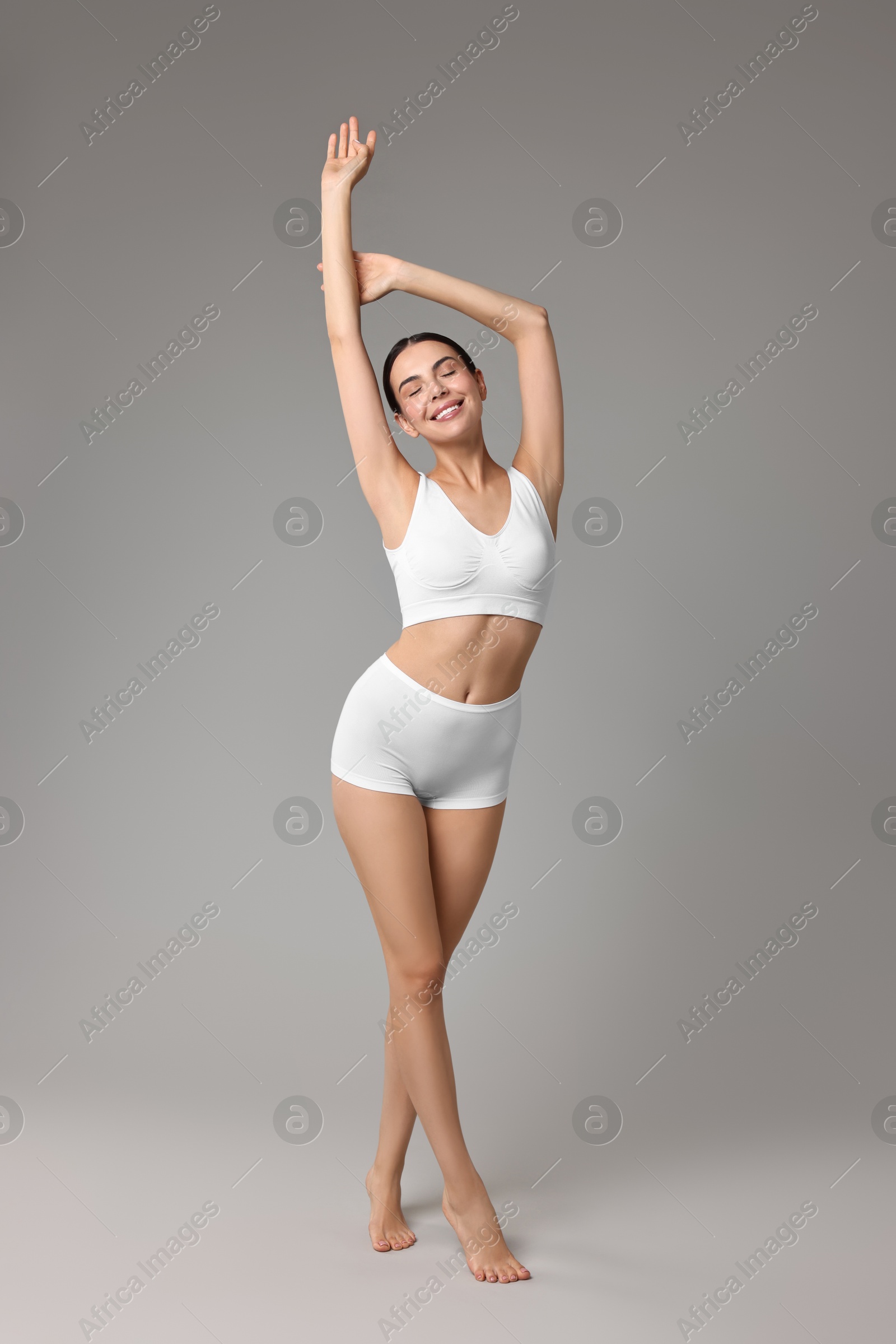 Photo of Smiling woman with perfect skin in underwear on grey background. Body care