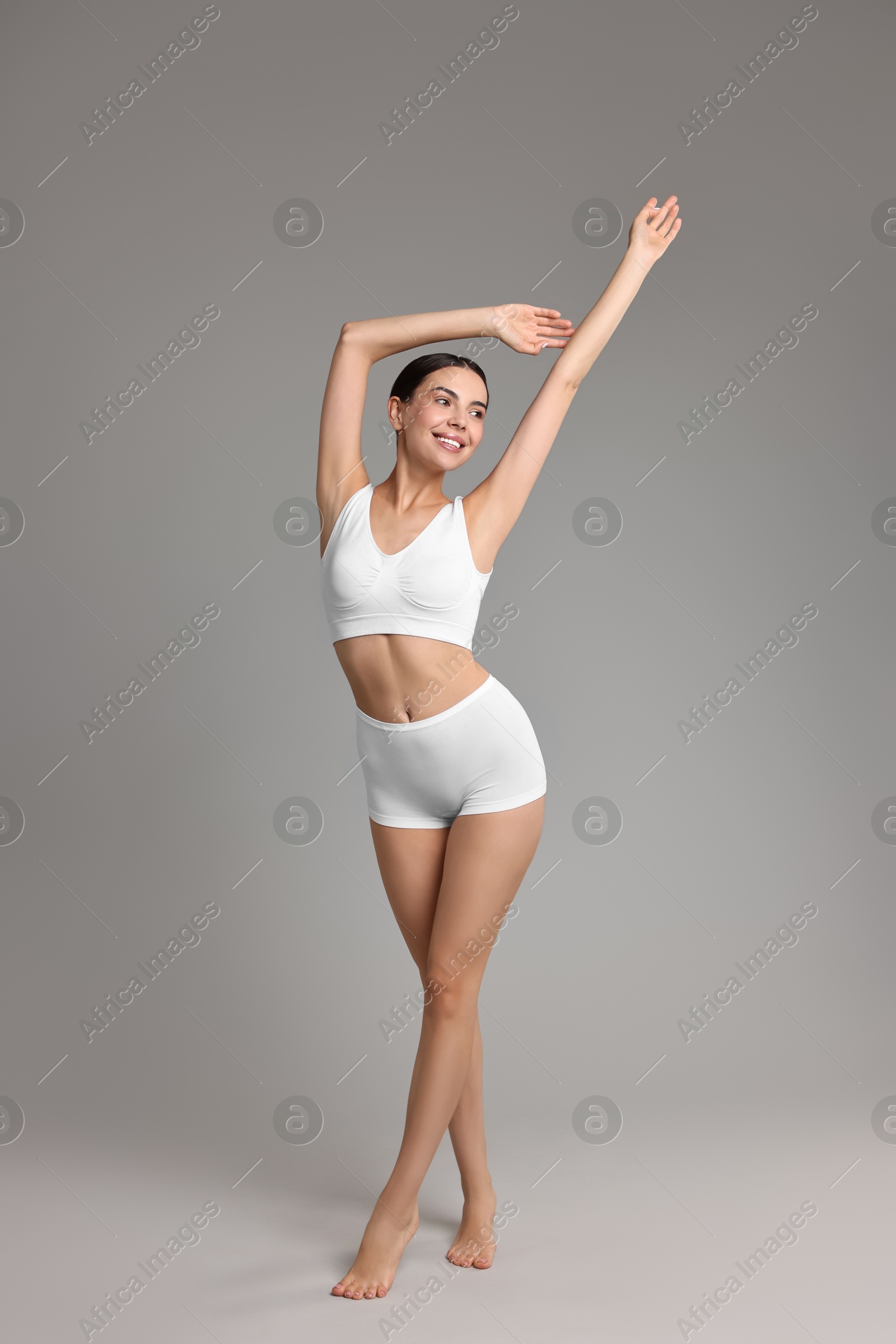 Photo of Smiling woman with perfect skin in underwear on grey background. Body care