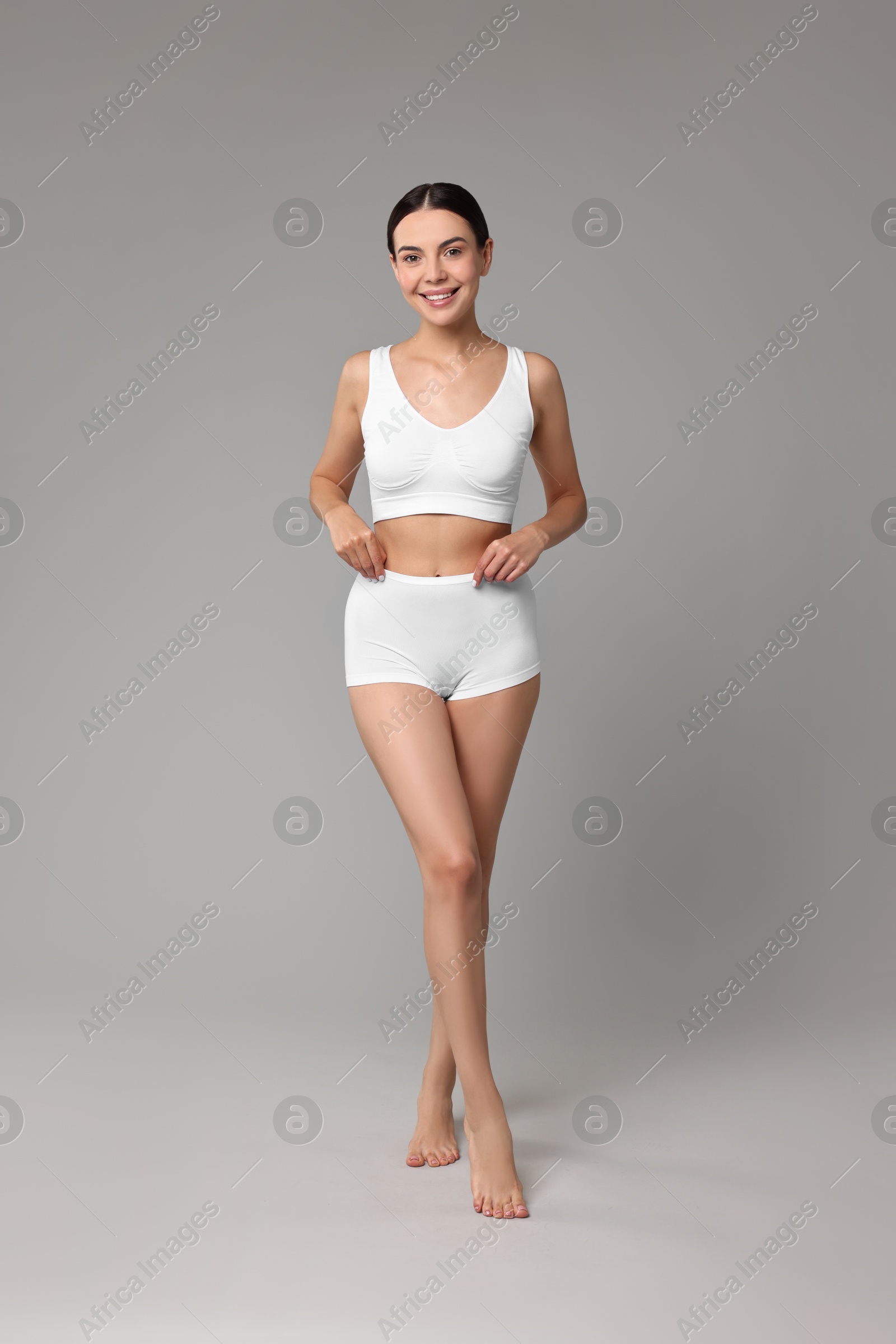 Photo of Smiling woman with perfect skin in underwear on grey background. Body care