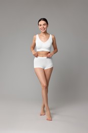 Photo of Smiling woman with perfect skin in underwear on grey background. Body care