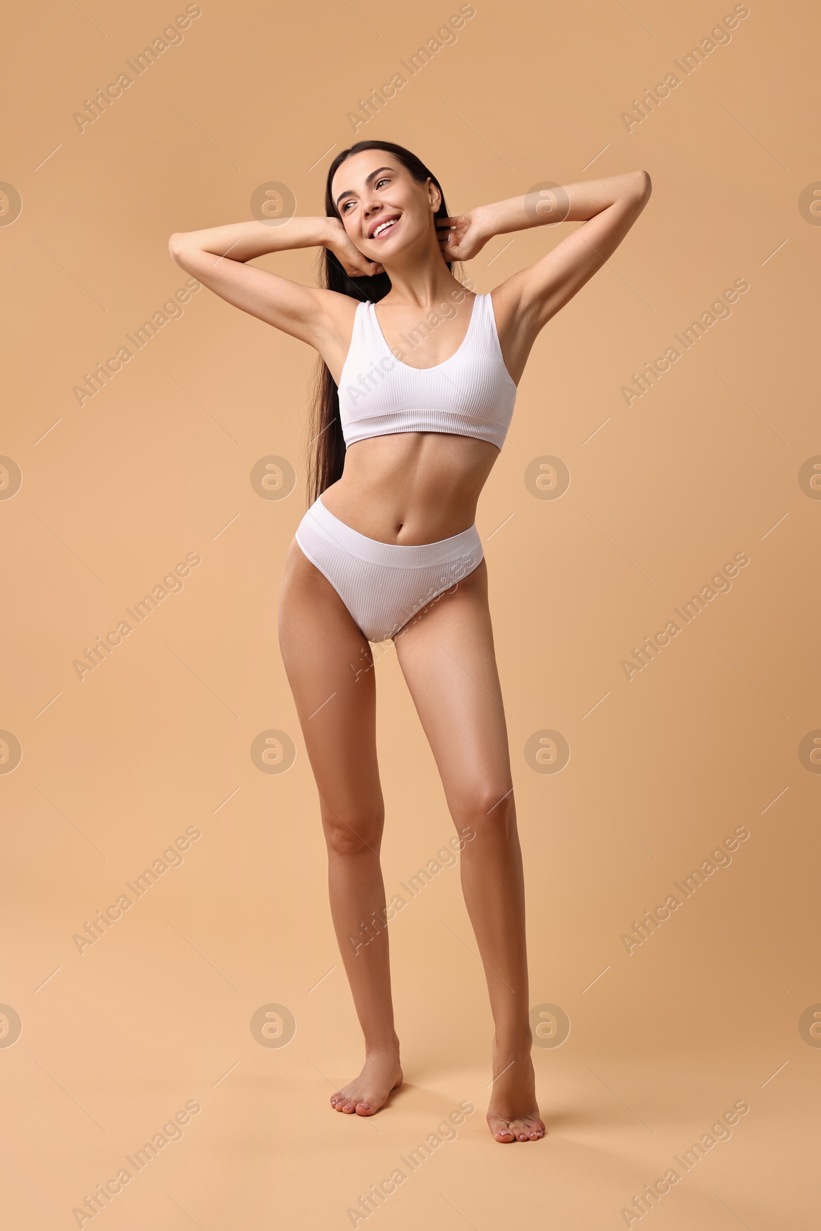 Photo of Smiling woman with perfect skin in underwear posing on beige background. Body care