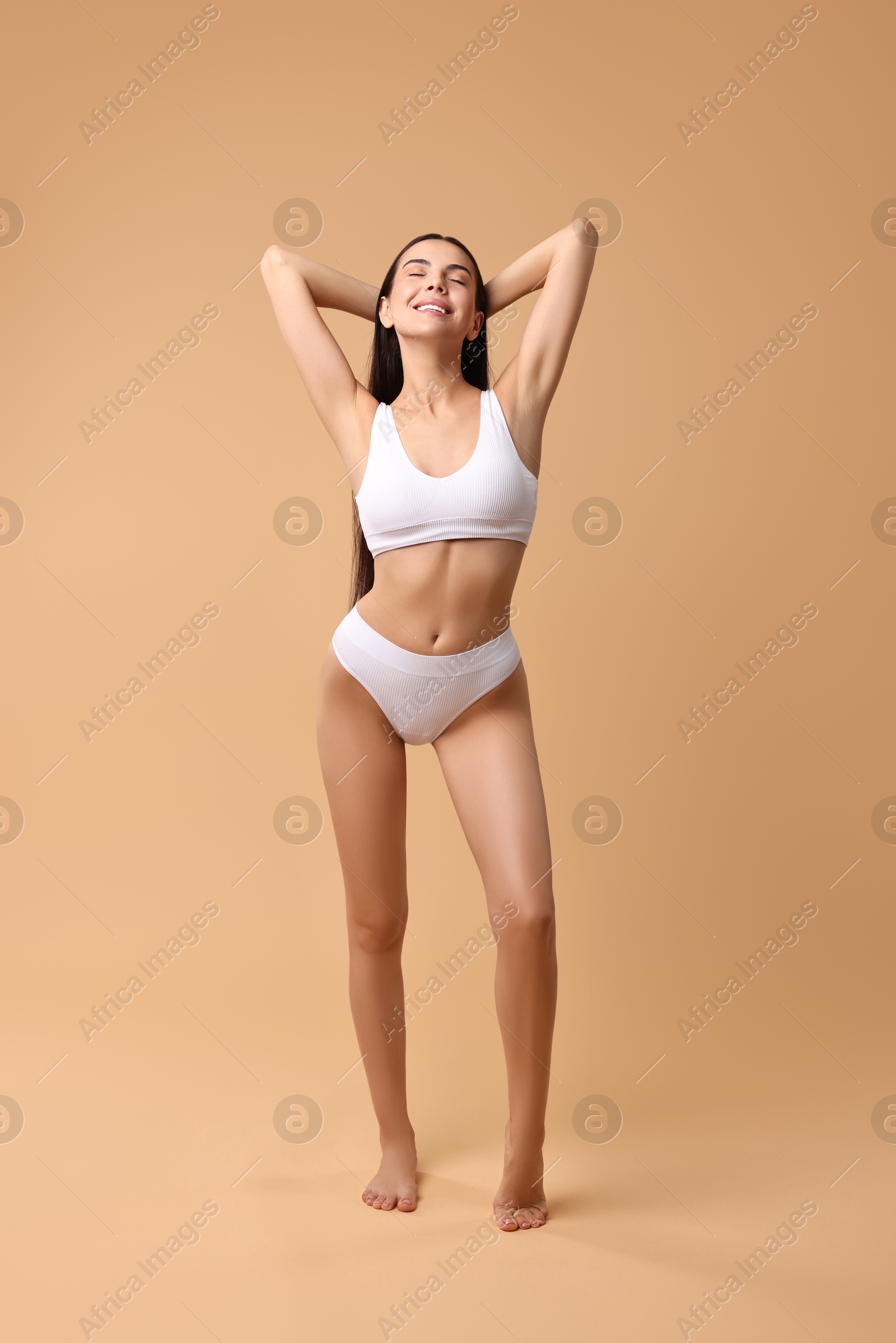 Photo of Smiling woman with perfect skin in underwear posing on beige background. Body care