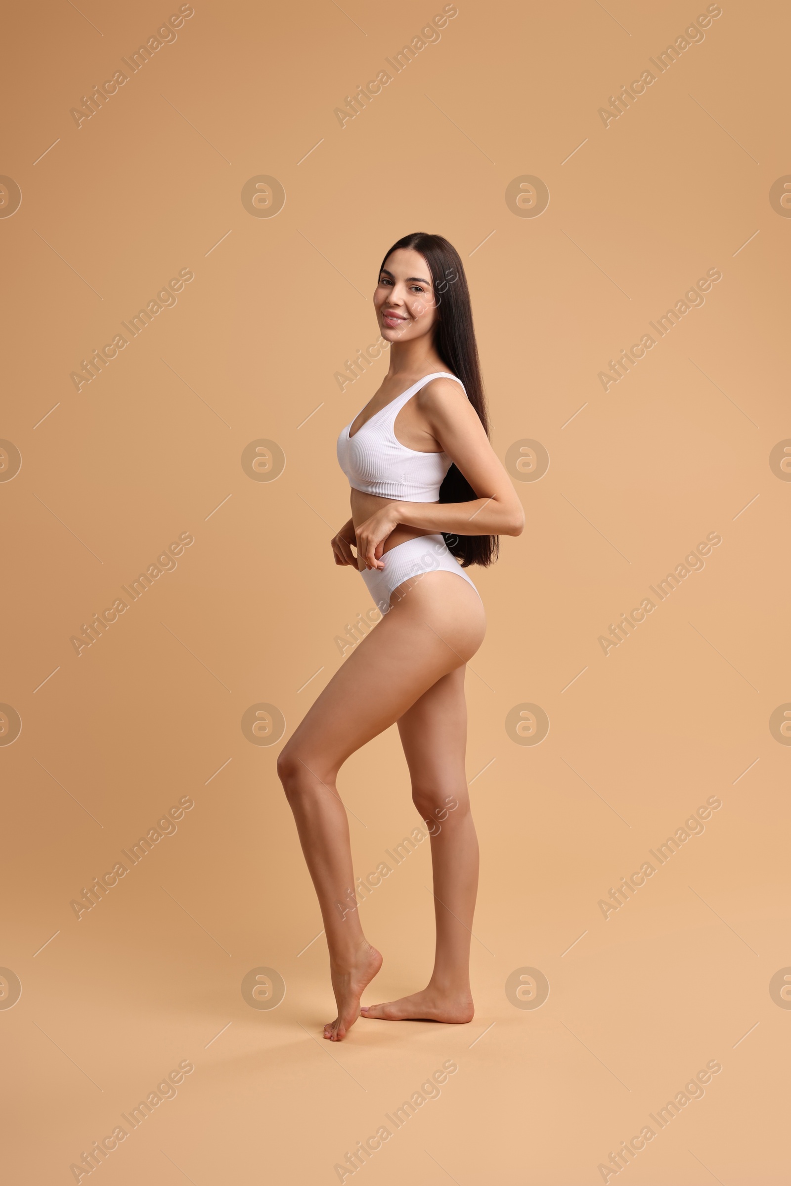 Photo of Smiling woman with perfect skin in underwear posing on beige background. Body care