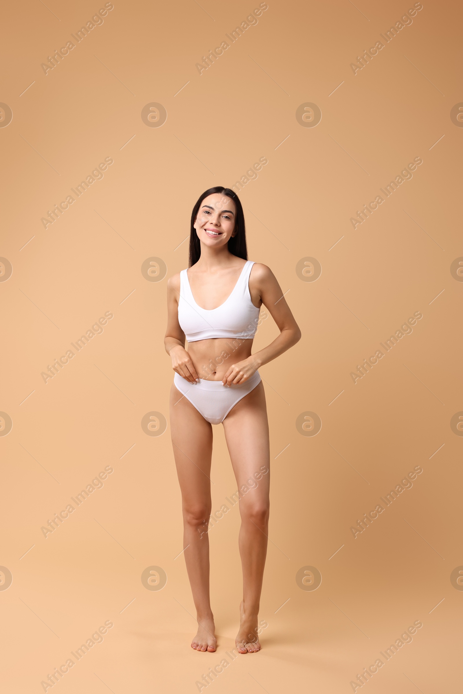 Photo of Smiling woman with perfect skin in underwear posing on beige background. Body care