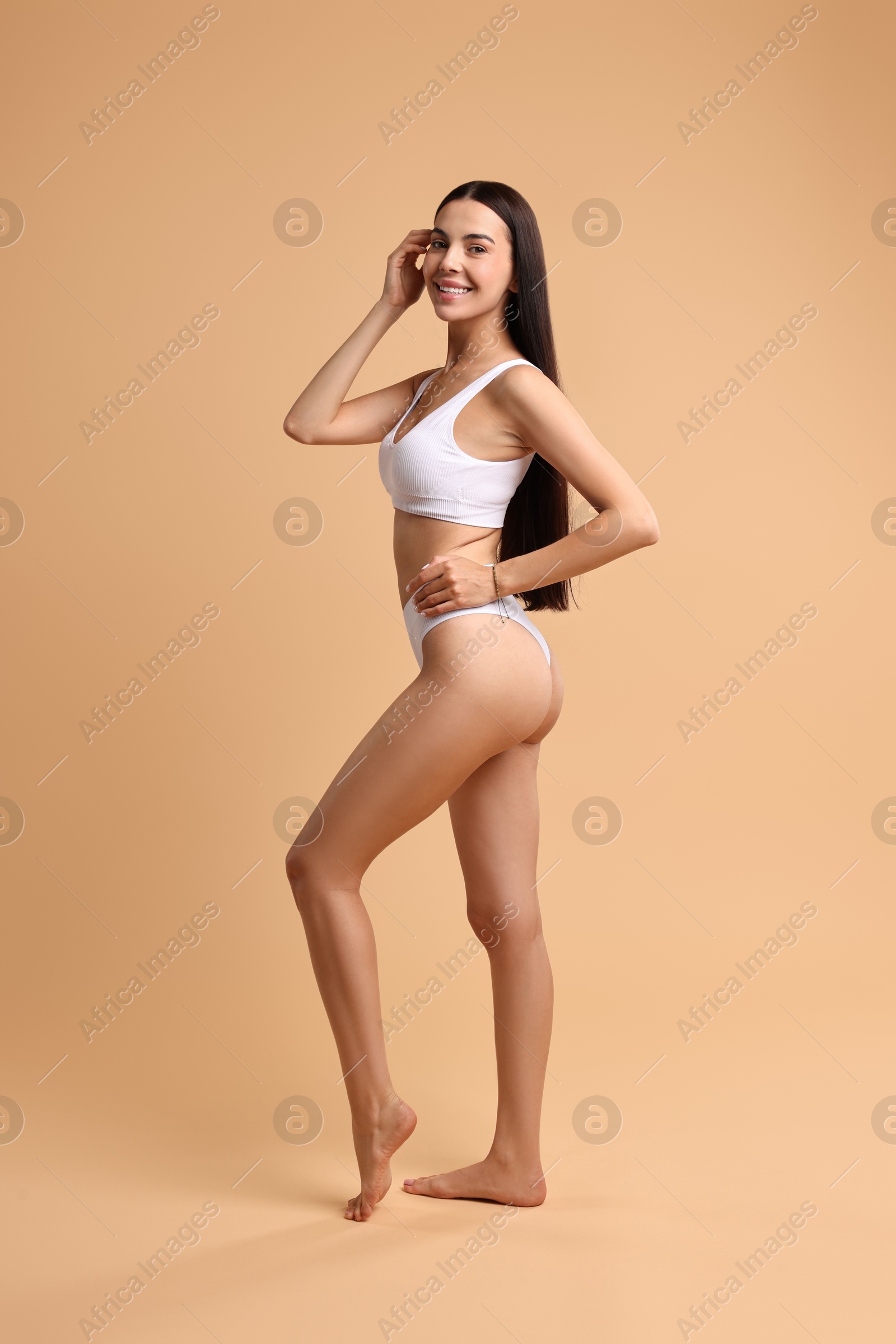 Photo of Smiling woman with perfect skin in underwear posing on beige background. Body care