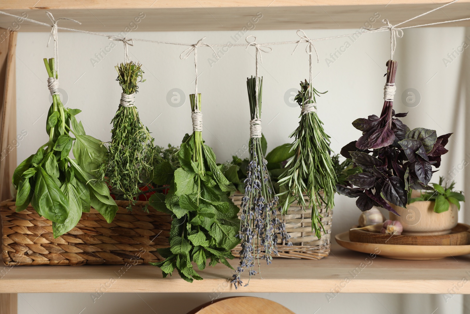 Photo of Bunches of different aromatic herbs hanging on rope indoors