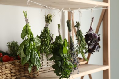 Photo of Bunches of different aromatic herbs hanging on rope indoors, closeup