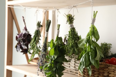 Photo of Bunches of different aromatic herbs hanging on rope indoors, closeup