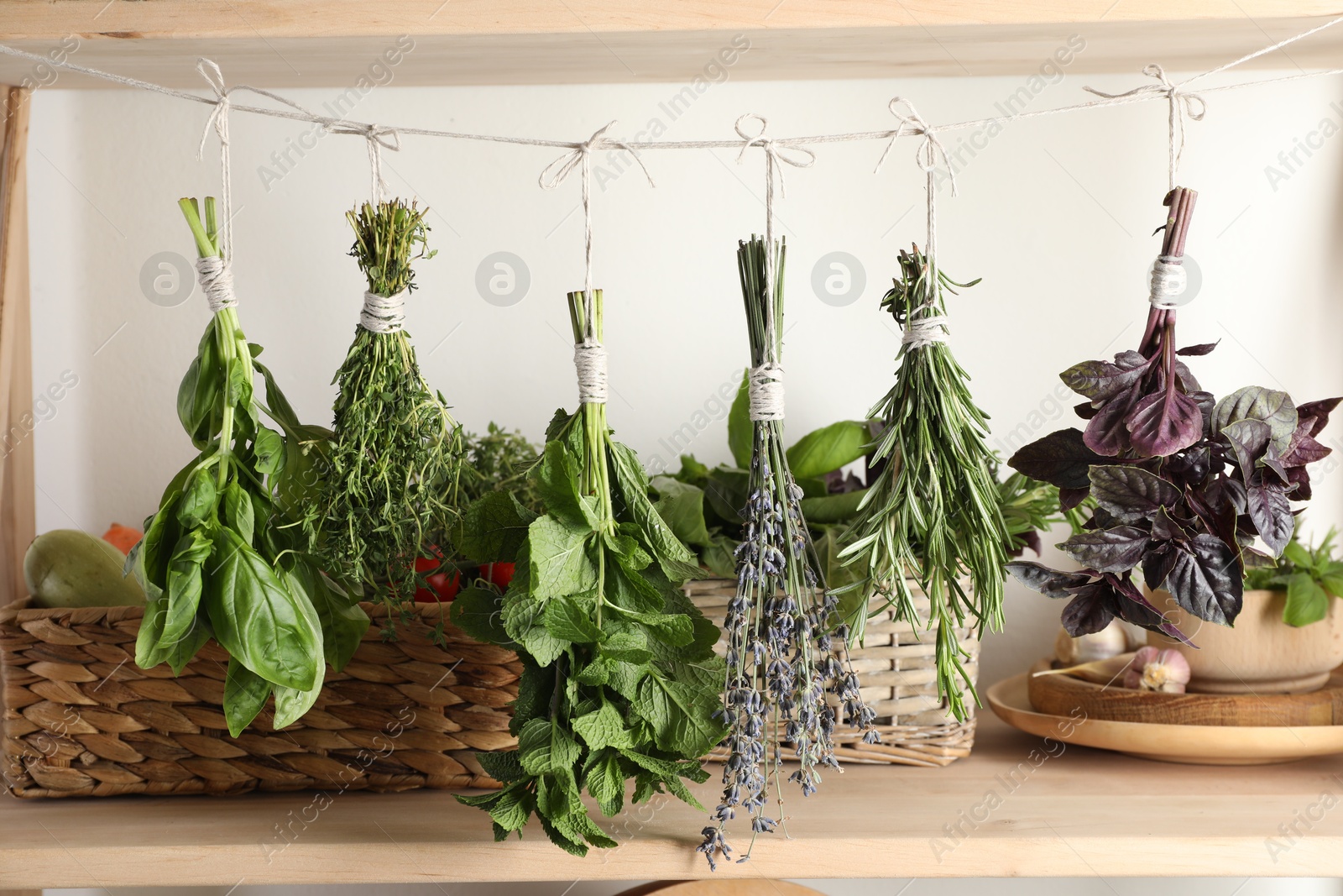 Photo of Bunches of different aromatic herbs hanging on rope indoors