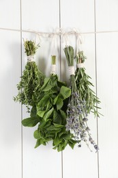 Bunches of different aromatic herbs hanging on rope near white wooden wall