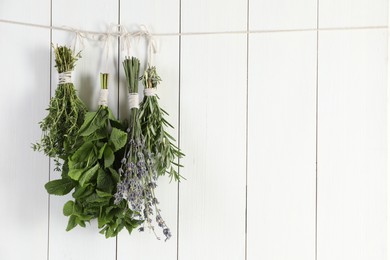 Bunches of different aromatic herbs hanging on rope near white wooden wall, space for text