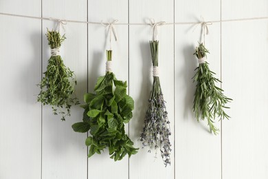 Bunches of different aromatic herbs hanging on rope near white wooden wall