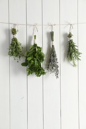 Photo of Bunches of different aromatic herbs hanging on rope near white wooden wall