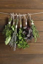 Photo of Bunches of different aromatic herbs hanging on rope near wooden wall