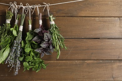 Photo of Bunches of different aromatic herbs hanging on rope near wooden wall, space for text