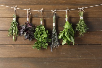 Photo of Bunches of different aromatic herbs hanging on rope near wooden wall