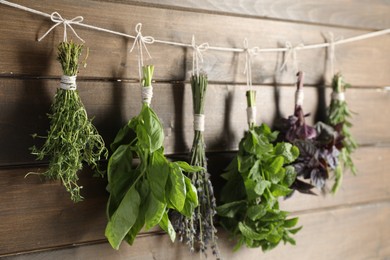 Photo of Bunches of different aromatic herbs hanging on rope near wooden wall, closeup