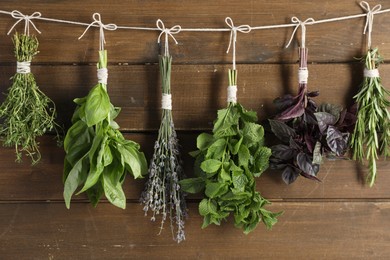 Photo of Bunches of different aromatic herbs hanging on rope near wooden wall